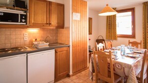 Una cocina con armarios de madera, microondas, lavavajillas y comedor con mesa para cuatro.