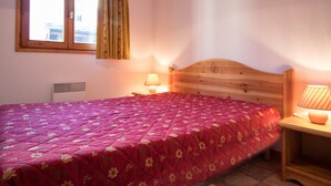 Un dormitorio con cabecera de madera, colcha estampada con motivos florales, dos lámparas de noche y una ventana con cortinas.