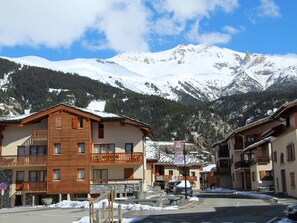 A mountain resort with wooden buildings, balconies, and a view of snow-covered peaks.