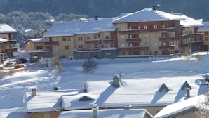 A multi-story hotel with balconies, a snow-covered landscape, and a mountainous backdrop. - Quiet apartment in Aussois, near shuttles and leisure (Aussois)