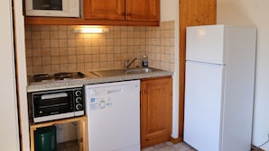 A compact kitchen with wooden cabinets, a microwave, a dishwasher, a stove, and a refrigerator. - Quiet apartment in Aussois, near shuttles and leisure (Aussois)