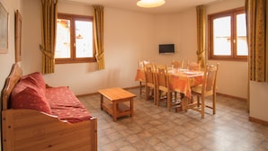 A room with a wooden bed, a dining table with chairs, a small wooden table, and a television on the wall. - Quiet apartment in Aussois, near shuttles and leisure (Aussois)