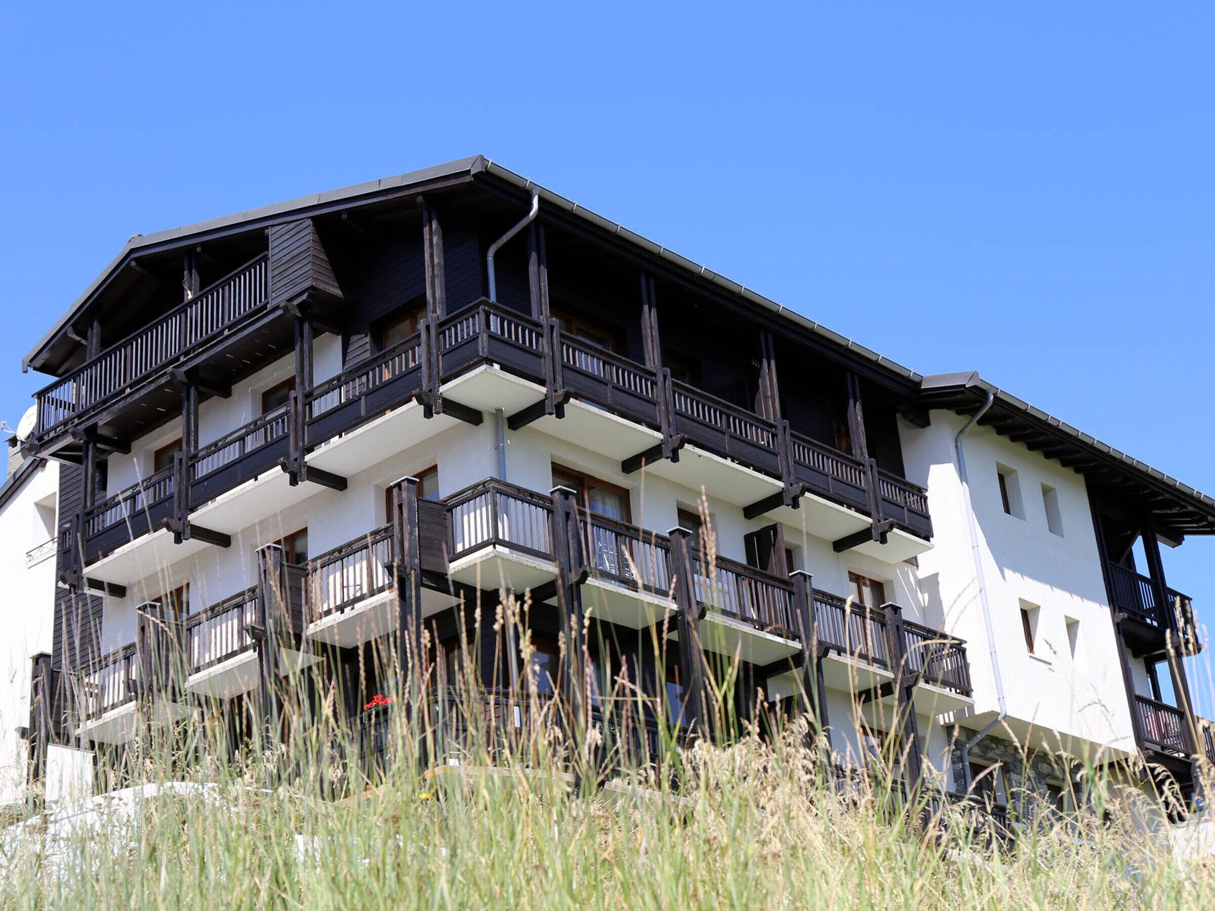 A multi-story building with balconies, white walls, and dark wooden railings.