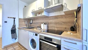 Une cuisine compacte équipée d’un lave-linge, d’un four et de meubles de rangement modernes.