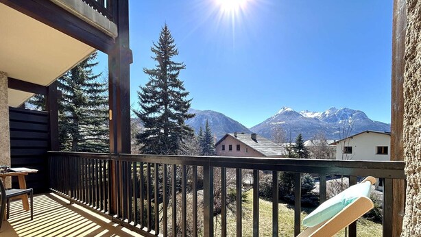 Une terrasse en bois avec une chaise, une table et une vue sur des montagnes enneigées.
