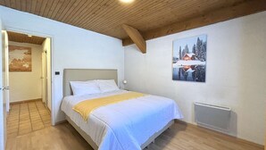 Une chambre avec un plafond en bois, un lit avec une literie blanche, un tableau représentant un paysage enneigé et un radiateur.