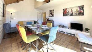 Un espace repas avec un plafond en bois, un sol carrelé et un téléviseur posé sur un meuble blanc.