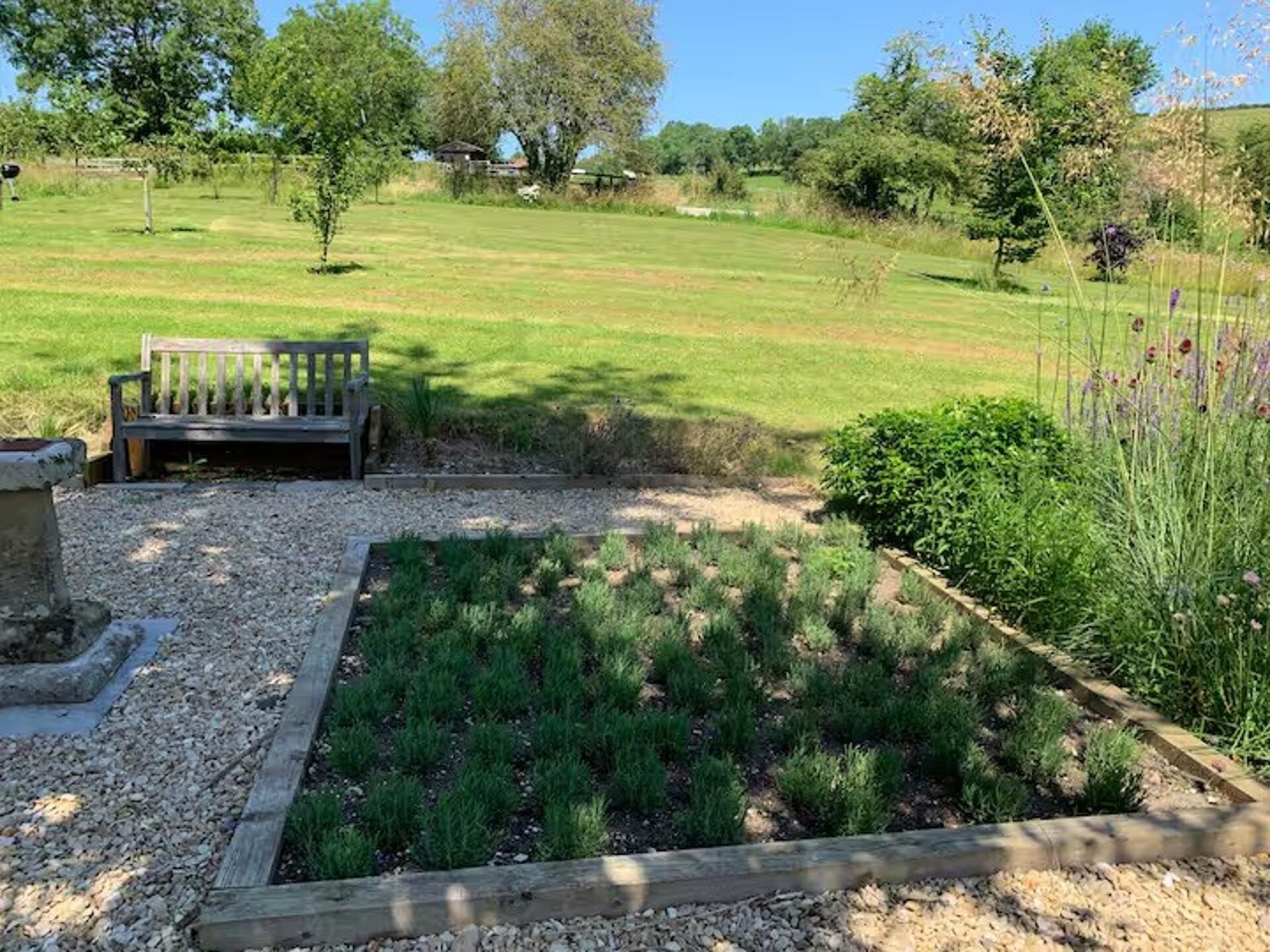 Un jardin avec un banc en bois, un parterre surélevé et, au fond, un champ d’herbe.