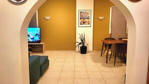 A living room with a TV, a dining table, and a potted plant. - Helios  Apartments (Rhodes)