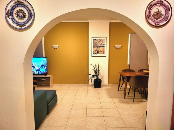 Uma sala de estar com televisão, mesa de jantar e planta em vaso.
