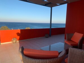 Een terras met rieten meubilair en uitzicht op zee.