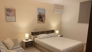 A bedroom with a bed, bedside tables, a lamp, a sofa, and a wall-mounted air conditioner. - Helios  Apartments (Rhodes)