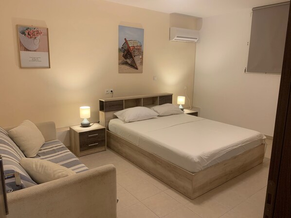 Un dormitorio con cama, mesitas de noche, lámpara, sofá y aire acondicionado instalado en la pared.