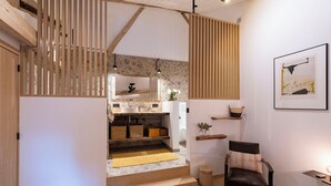 A modern interior with a staircase leading to a kitchen area, wooden beams, and a framed artwork on the wall.