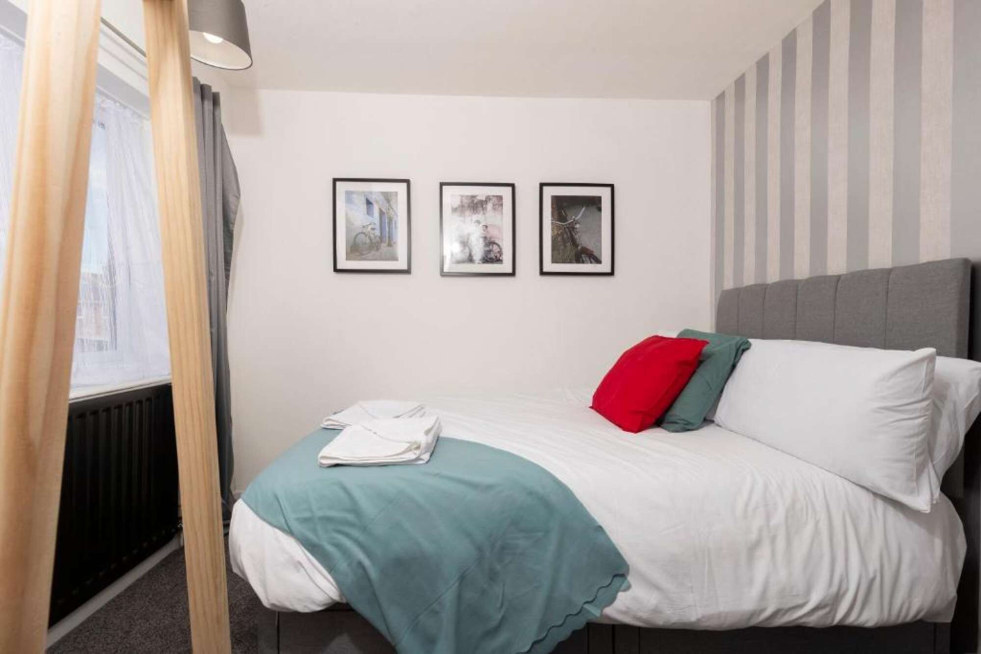 A hotel room with a bed, a window with curtains, and three framed pictures on the wall.