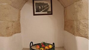 Un arc en pierre surmonté d’un tableau encadré. Sous l’arc, on trouve une étagère en pierre sur laquelle repose un plateau en métal contenant des fruits.