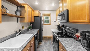 A kitchen with granite countertops, wooden cabinets, a refrigerator, stove, microwave, and a coffee maker. - Grandma's Hideaway - walk to downtown, private hot tub, pet friendly with patio (McCall)
