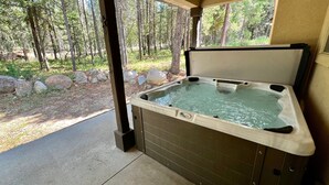 A hot tub with a wooden exterior, set in a covered area with a view of a forested area. - Grandma's Hideaway - walk to downtown, private hot tub, pet friendly with patio (McCall)