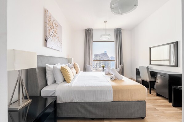 A modern hotel room with a large bed, a desk, and a view of the city.