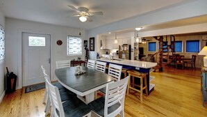 A spacious kitchen with a central island, wooden flooring, and a dining area with white chairs. - Sandpiper Cottage - Ocracoke Island (Ocracoke)