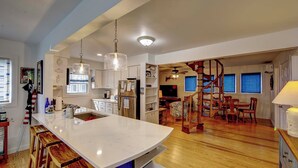 A modern kitchen with a large island, wooden bar stools, and pendant lighting. - Sandpiper Cottage - Ocracoke Island (Ocracoke)