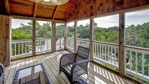 A covered porch with wooden railings, wicker furniture, and a view of a forested landscape. - Sandpiper Cottage - Ocracoke Island (Ocracoke)