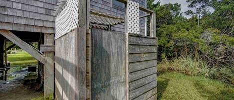A rustic wooden structure with a lattice window and a door, surrounded by natural vegetation.
