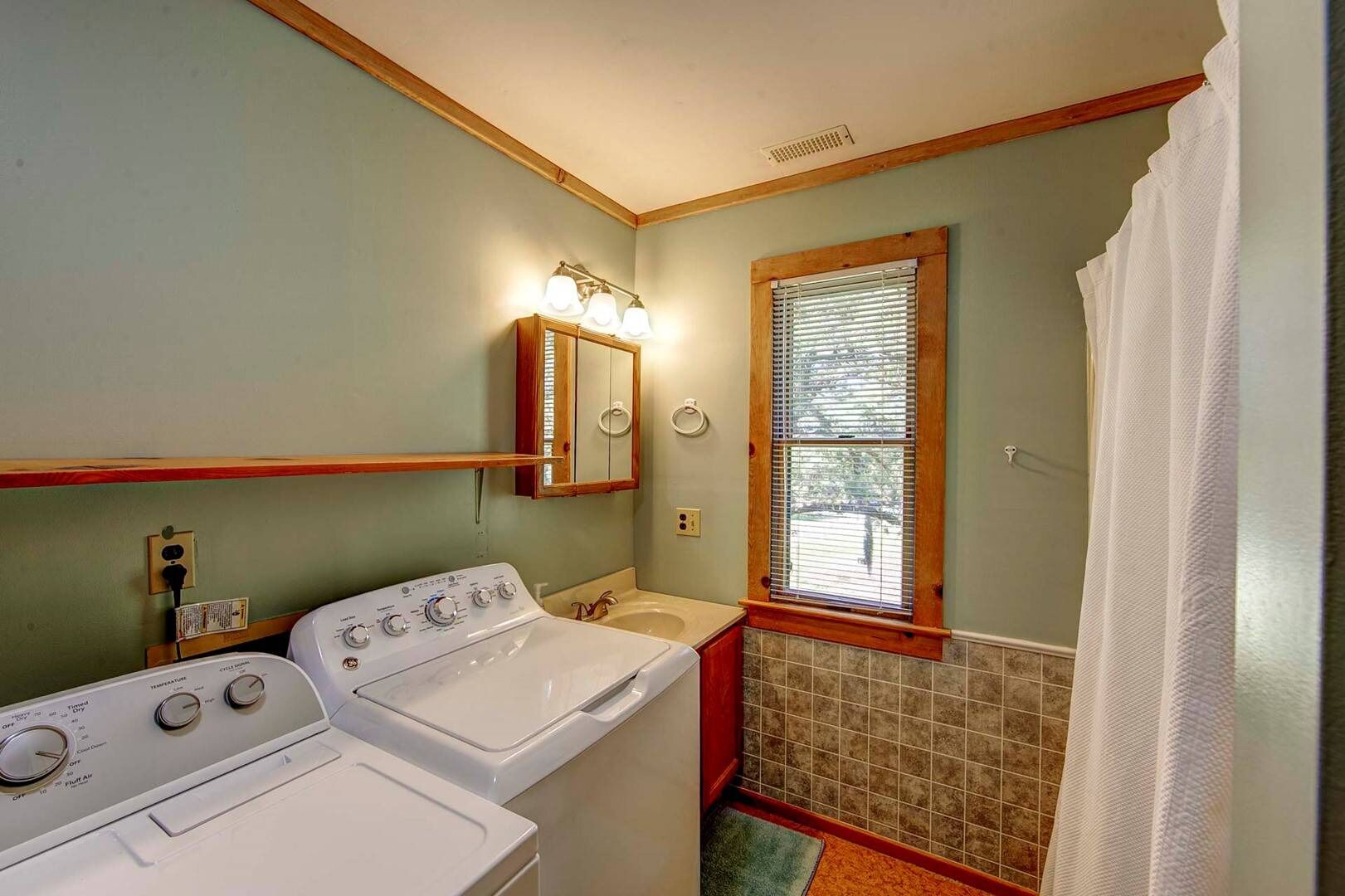 A compact bathroom with a washing machine, a sink, and a window with blinds.