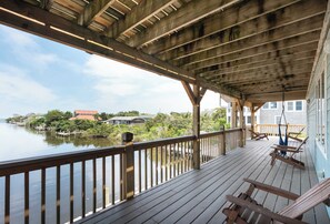 Une terrasse en bois avec une balustrade donnant sur un plan d’eau, une chaise suspendue et un hamac.