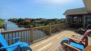 En træterrasse med stole, med udsigt over et roligt vandareal, omgivet af huse og grøn bevoksning.