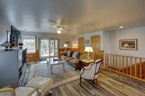 Relax in this spacious living room with a high ceiling, ceiling fan, and large window offering a view of the outdoors.
