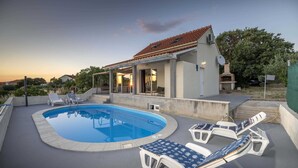 Ein Schwimmbad mit Liegestühlen, einer überdachten Terrasse und einem Gebäude mit einem Ziegeldach.