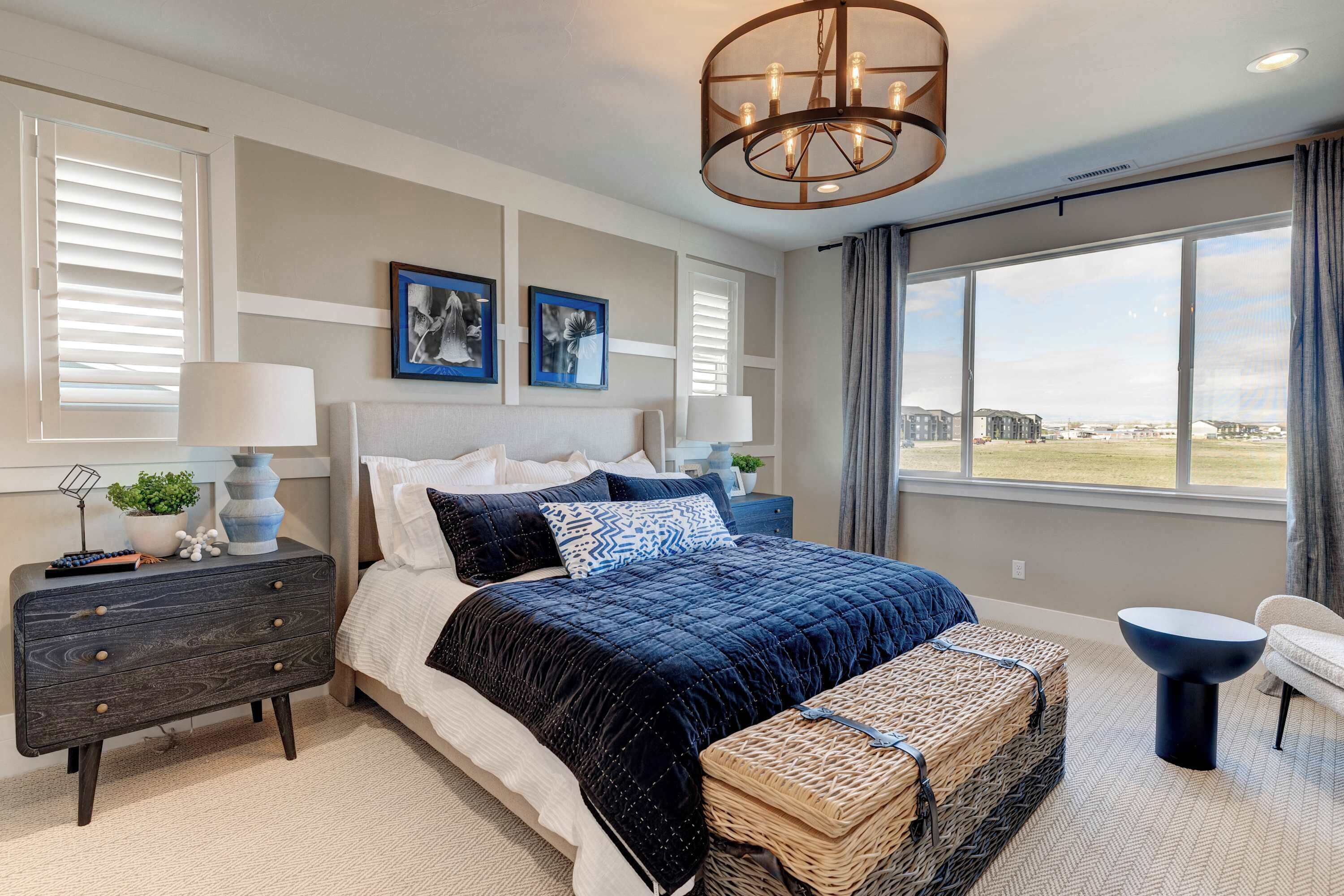 A bedroom with a large bed, a nightstand, a dresser, a bench, and a view of the outdoors.