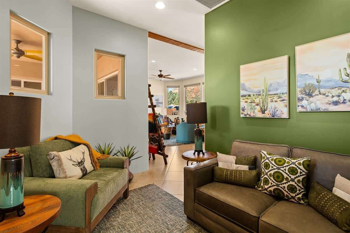 A living room with two sofas, a coffee table, and a lamp. There are paintings on the wall and a ceiling fan.