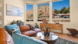 A living room with a leather couch, a glass coffee table, and a view of a mountain landscape through large windows.