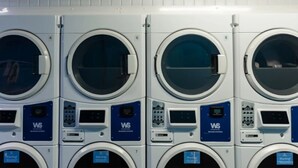 A row of front-loading washing machines with control panels and warning labels. - Prince Consort Village (London)
