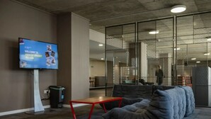A modern lounge area with a large flat-screen TV, a red table, and a grey sofa. - Prince Consort Village (London)