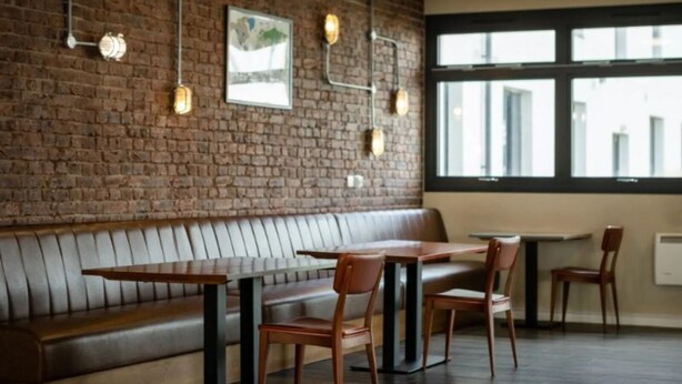 A restaurant interior with a brick wall, wooden tables and chairs, and a large window. - Prince Consort Village (London)