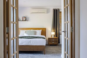 Habitación de hotel con cama de madera, mesita de noche con lámpara, aire acondicionado de pared y ventana con cortinas.