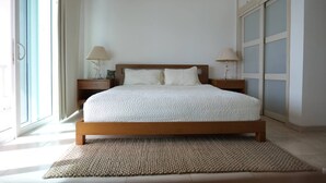 A bedroom with a wooden bed, two bedside tables with lamps, a large window, and a view of the outside.