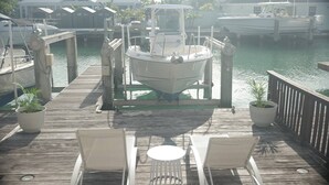 A dock with a boat, two lounge chairs, and potted plants.