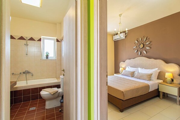 A hotel room with a bathroom, a bed with a headboard, and a nightstand with a lamp.