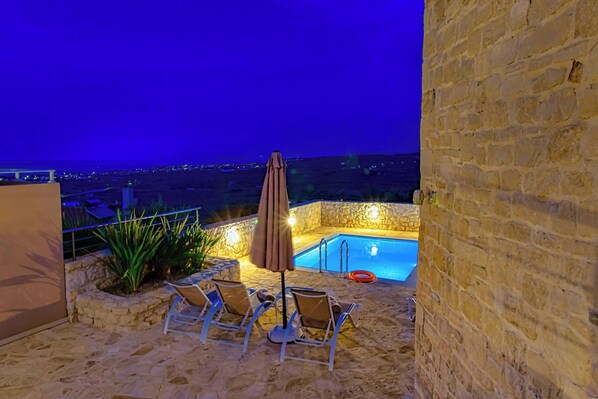 A stone patio with a pool, lounge chairs, and an umbrella.