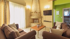 A living room with a stone fireplace, a flat-screen TV, and a green accent wall. - Amoena Villa - Theo Villas With Sea View (Marathokefala)