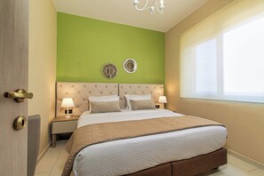 A neatly arranged bedroom with a large bed, two bedside tables with lamps, a green accent wall, and a window with a view.