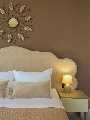 A neatly made bed with white and beige bedding, a decorative wall piece above it, and a bedside lamp on a nightstand.