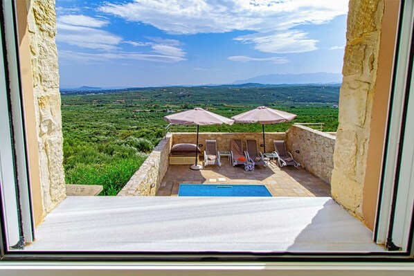 A balcony with a pool, lounge chairs, and umbrellas overlooking a green landscape.