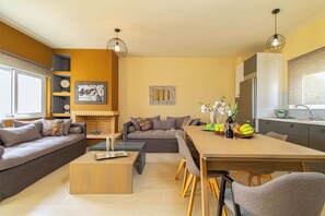 Een moderne woonkamer met een bank, salontafel en eettafel. Er is een keuken met een koelkast en spoelbak.