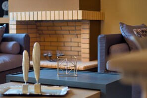 Een moderne woonkamer met een bakstenen openhaard, twee leren banken en een salontafel met decoratieve objecten.