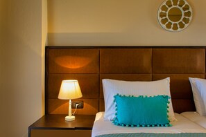 A neatly made bed with a teal pillow and a white pillow, a bedside lamp, and a decorative wall piece.